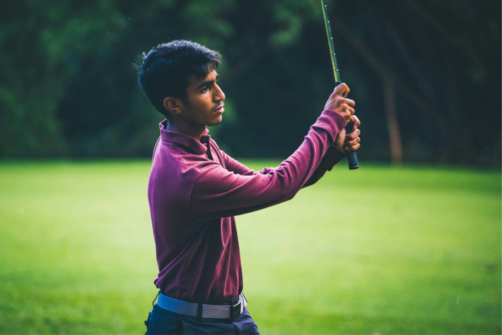 A young man in a maroon shirt has just completed a swing of a golf club.