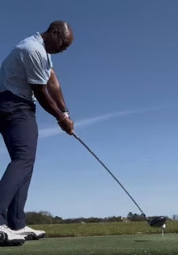 Cedric Davis stands in golf attire preparing to swing a golf club on a clear day.